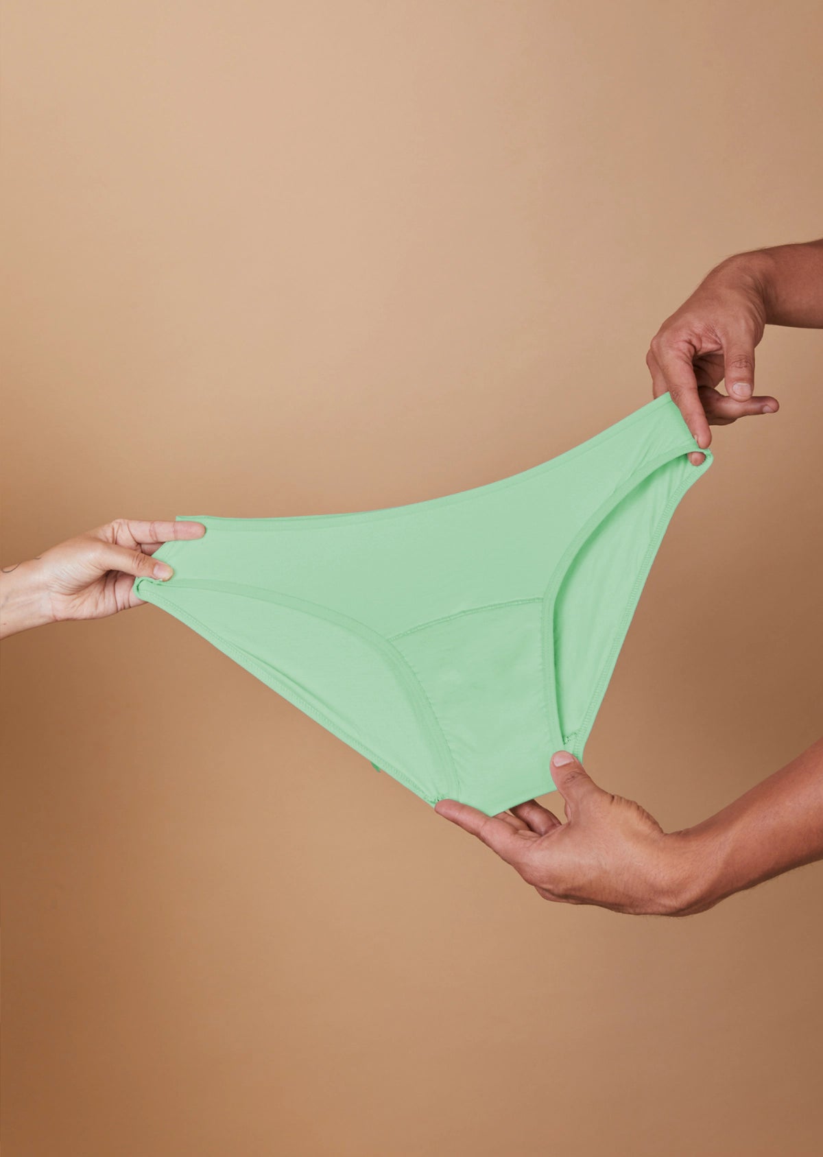 Green underwear held between two hands against a beige background