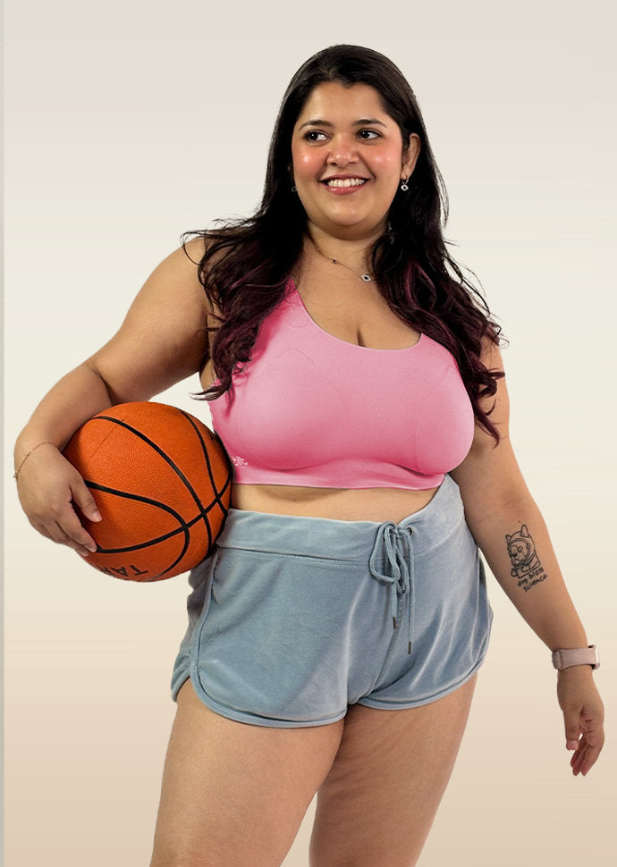 Woman holding a basketball wearing a pink bra and light blue shorts on a plain background