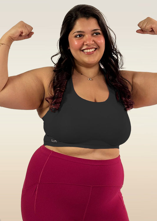 Woman flexing her muscles wearing a black sports bra and pink leggings on a white background