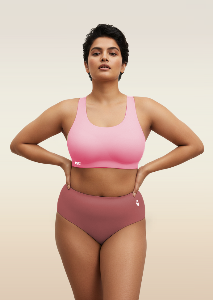 Woman wearing a pink sports bra and mid-waist pink underwear on a beige background