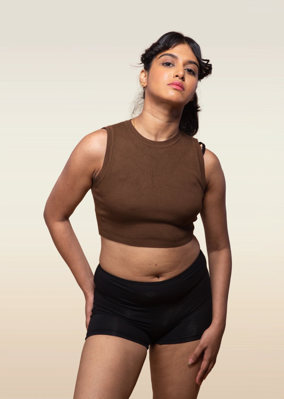 Woman wearing a brown sleeveless top and black boyshorts against a beige background