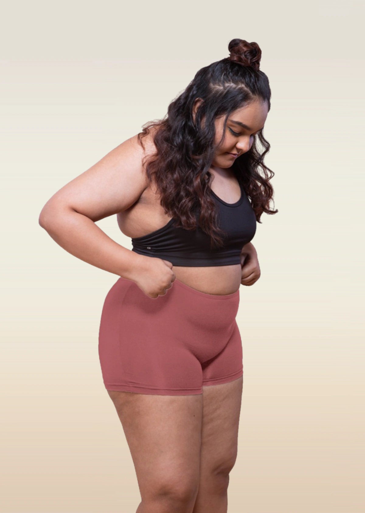Woman wearing a black sports bra and red boyshorts on a beige background