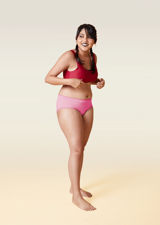 Woman wearing a red sports bra and pink underwear on a beige background