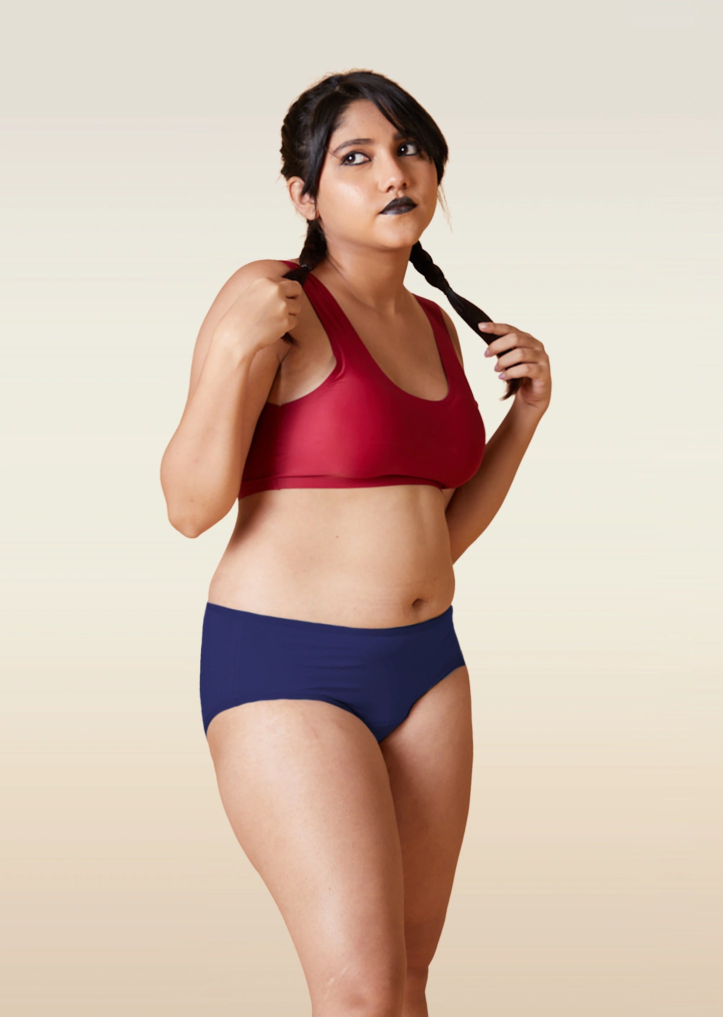 Woman wearing a red sports bra and blue breifs on a beige background