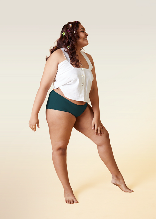 Woman wearing a white top and teal underwear on a beige background