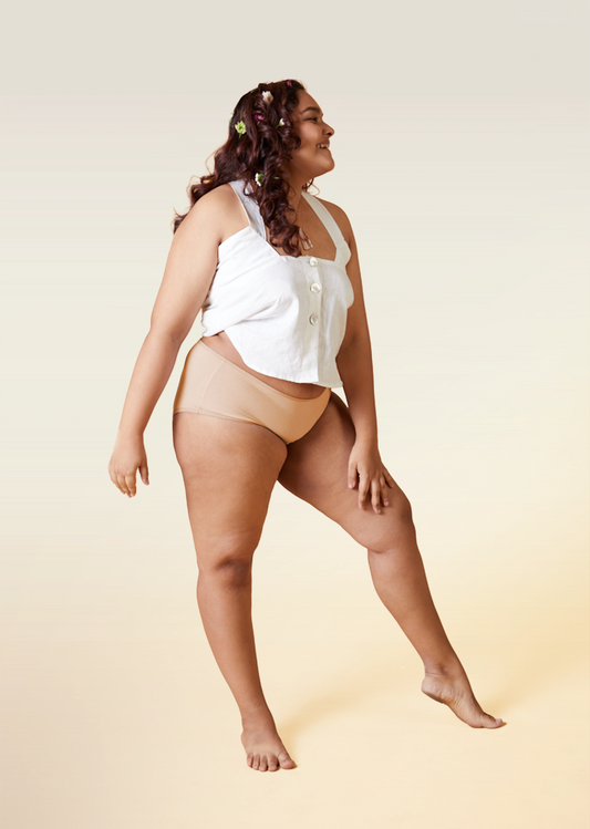 Woman wearing a white top and beige underwear on a beige background