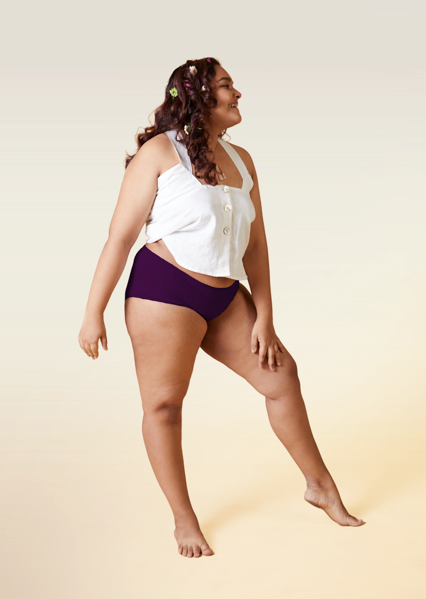 Woman wearing a white top and violet mid-waist underwear on a beige background