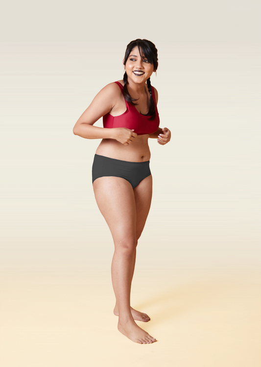 Woman wearing a red sports bra and grey underwear on a beige background