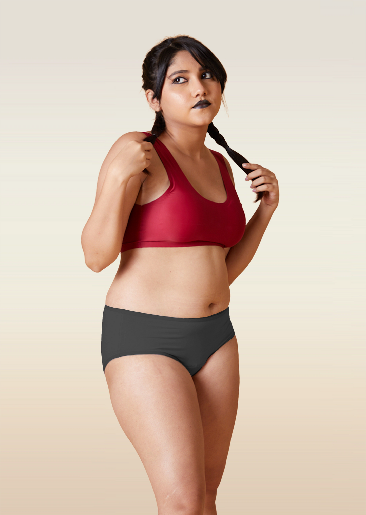 Woman wearing a red sports bra and grey underwear on a beige background