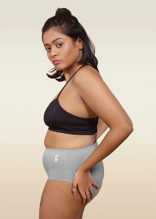 Woman wearing a black sports bra and gray mid-waist underwear on a beige background