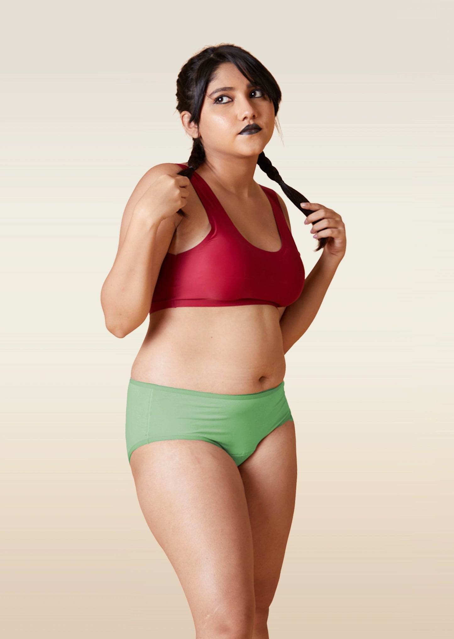 Woman wearing a red sports bra and green shorts against a beige background