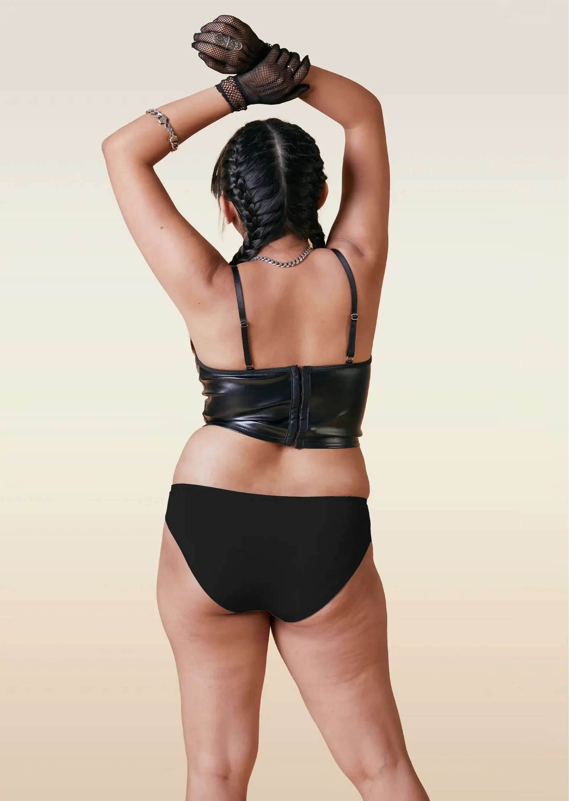 Person wearing a black leather outfit and black underwear with a beige background