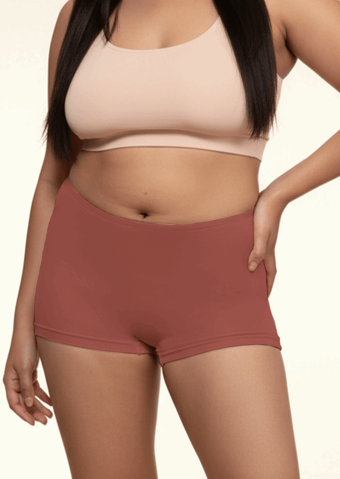 Person wearing a beige sports bra and red boyshorts on a plain background