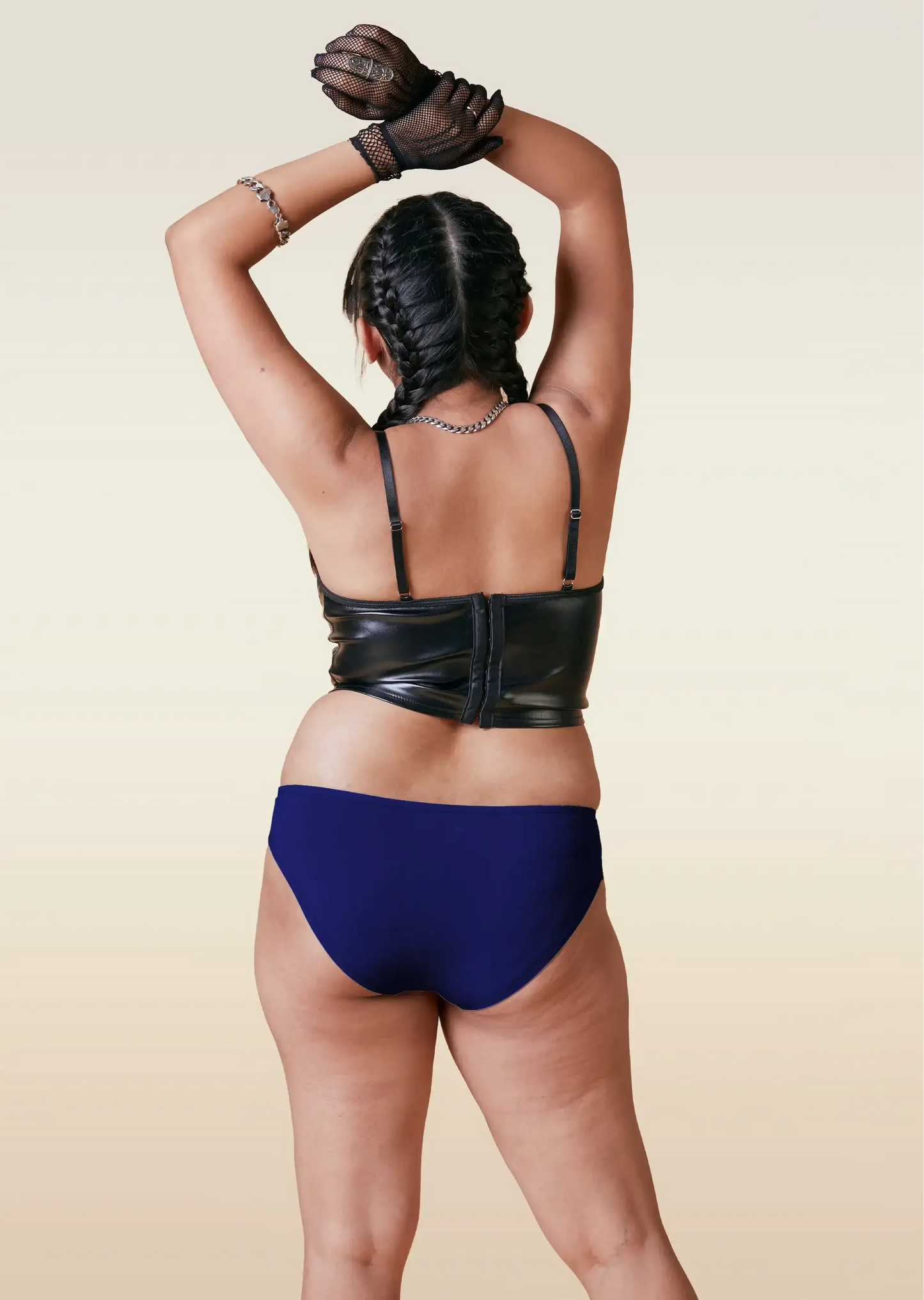 Person wearing a black leather top and blue underwear on a beige background