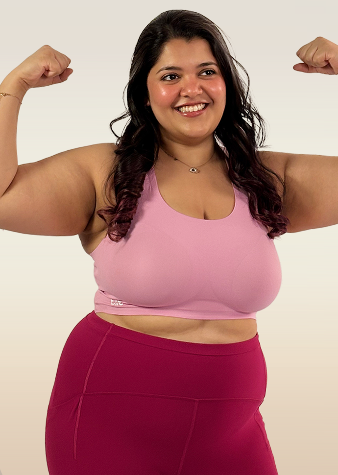 Woman flexing her muscles wearing a pink sports bra and maroon leggings on a white background