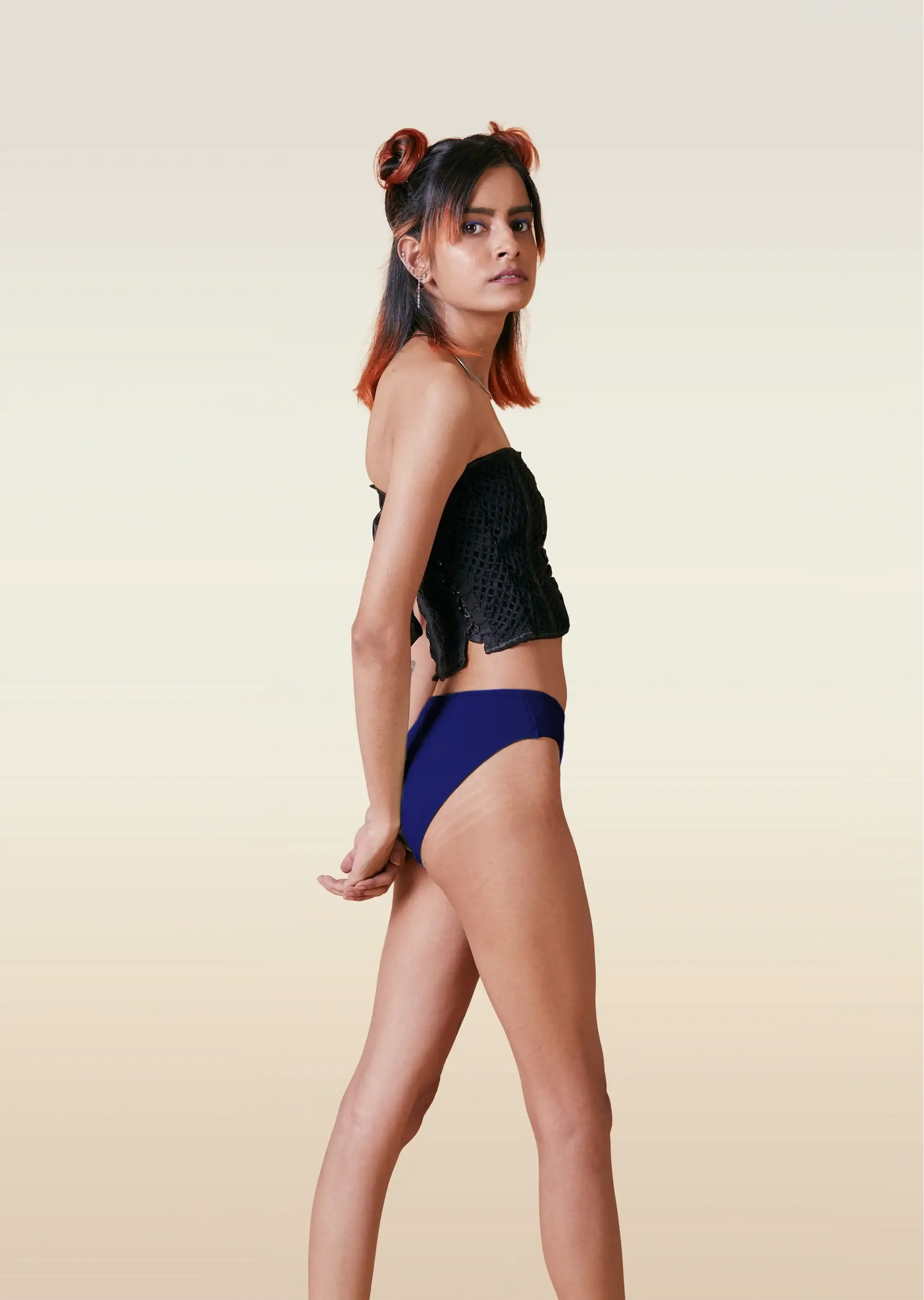 Woman wearing a black top and blue low-waisted bikini bottoms on a beige background