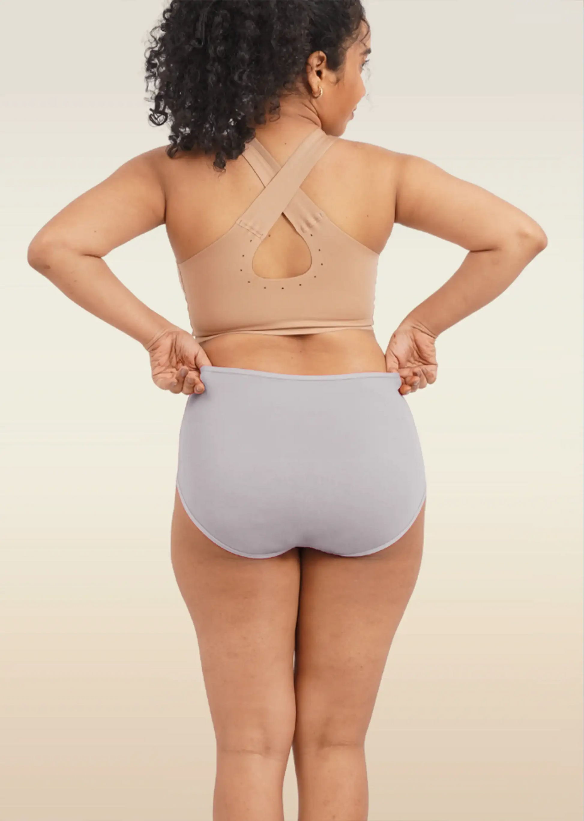 Person wearing a beige sports bra and light underwear on a plain background