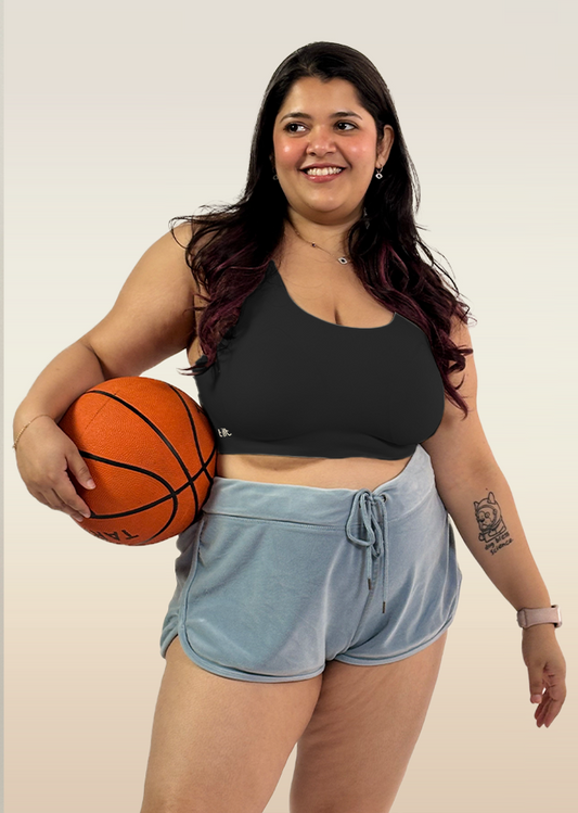 Woman holding a basketball wearing a black sports bra and light blue shorts on a plain background