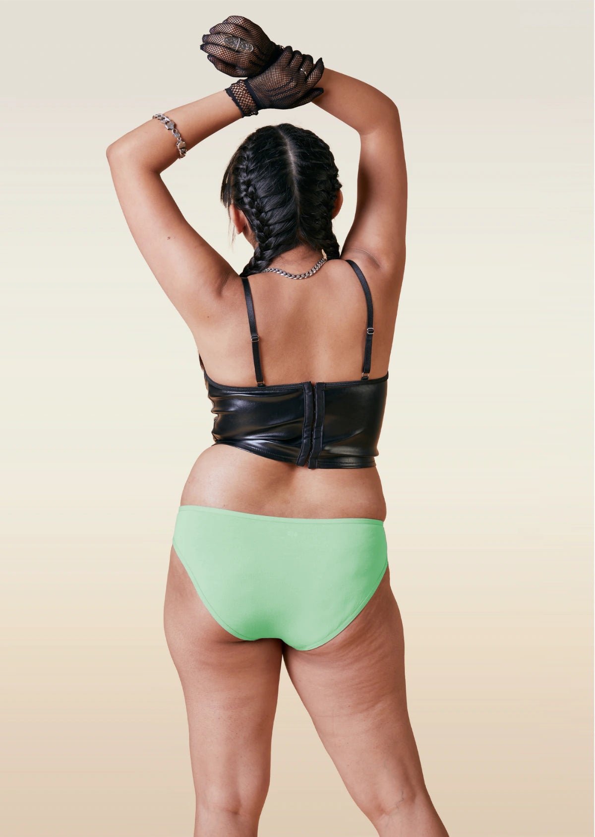 Person wearing a black leather top and green bikini underwear on a beige background