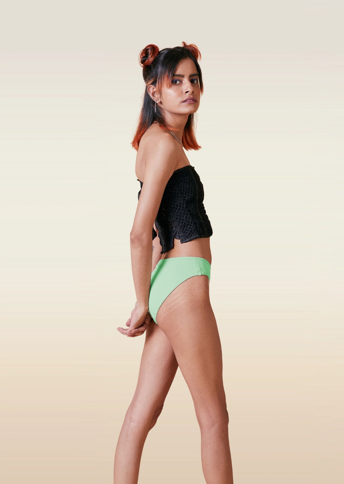 Woman wearing a black top and green  bikini underwear on a beige background