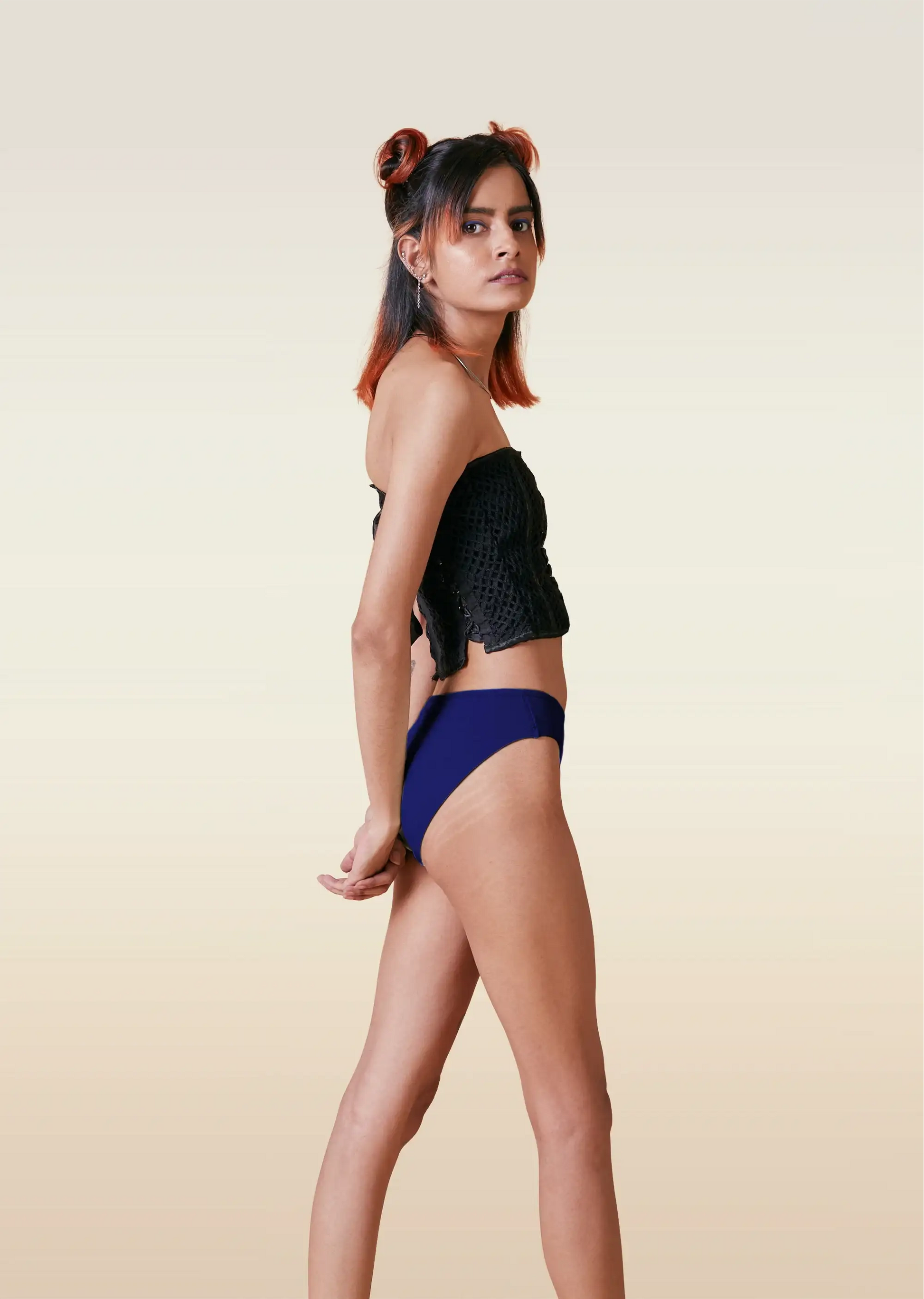 Woman wearing a black top and blue low-waisted bikini bottoms on a beige background