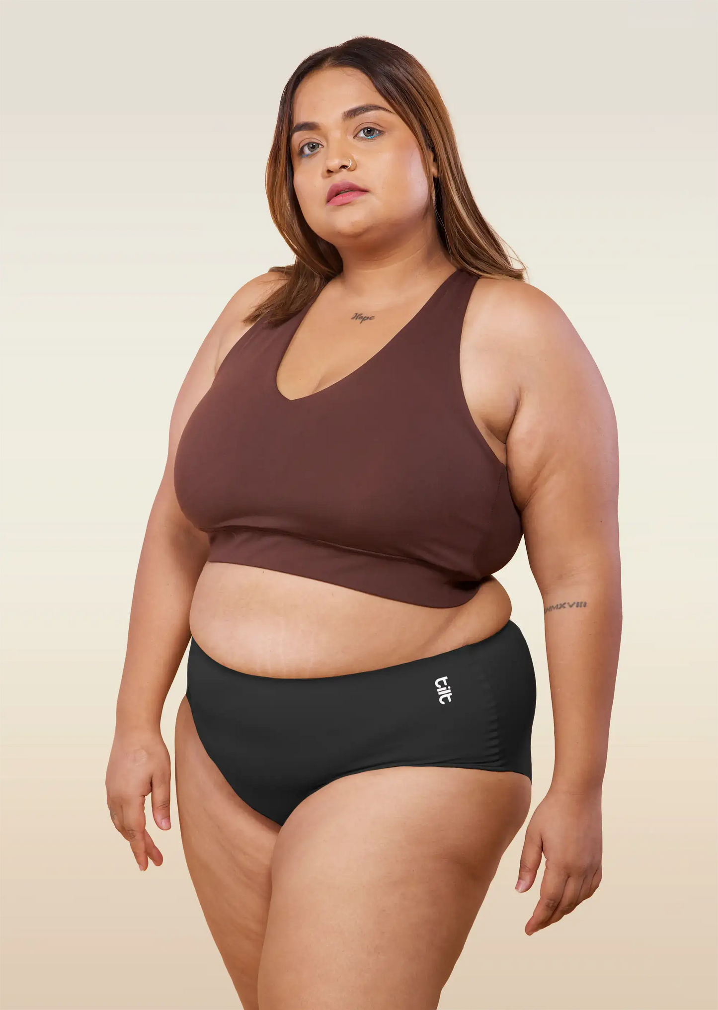 Woman wearing a brown sports bra and black mid-waist underwear on a beige background