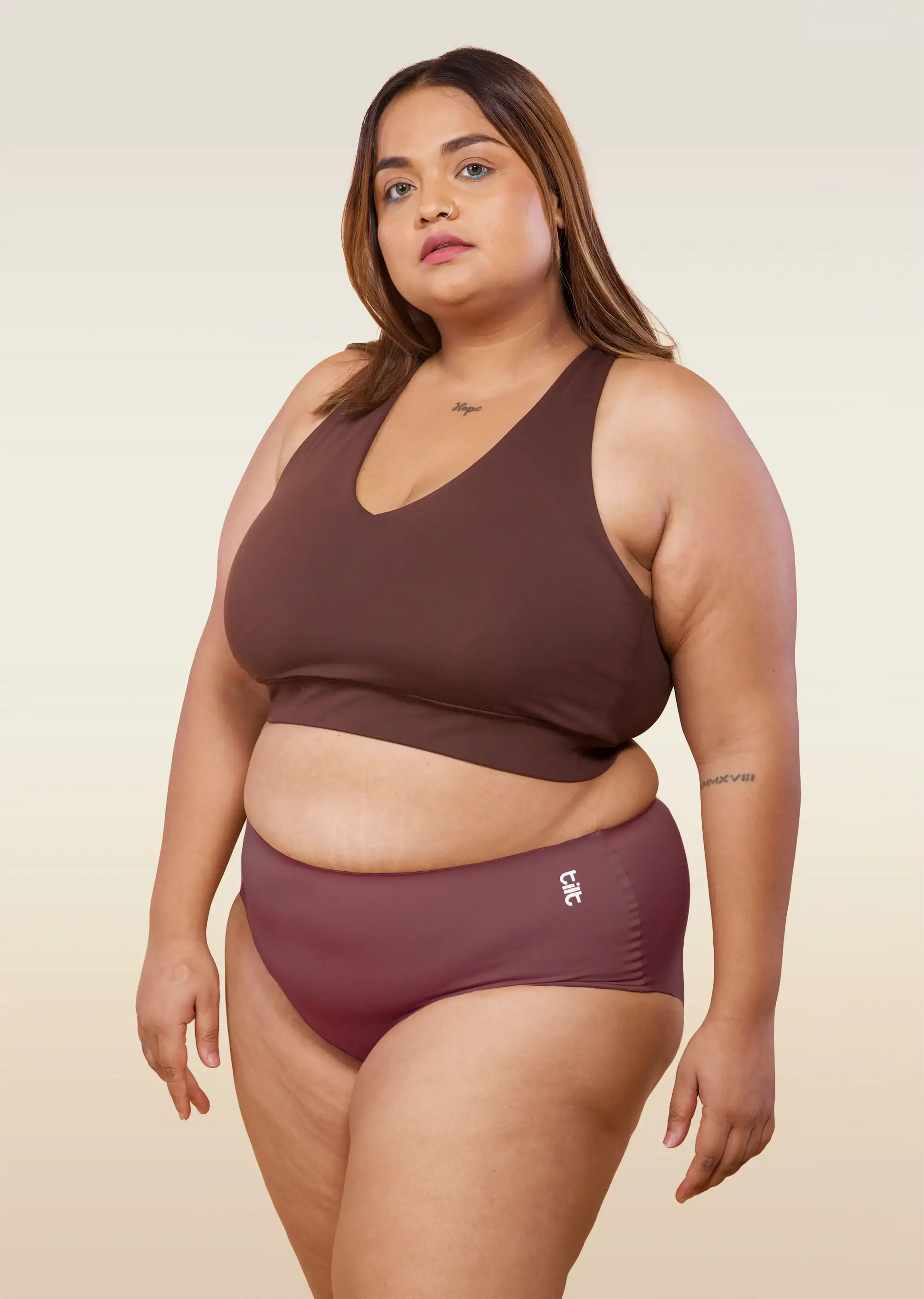 Woman wearing a brown bra and pink underwear on a beige background