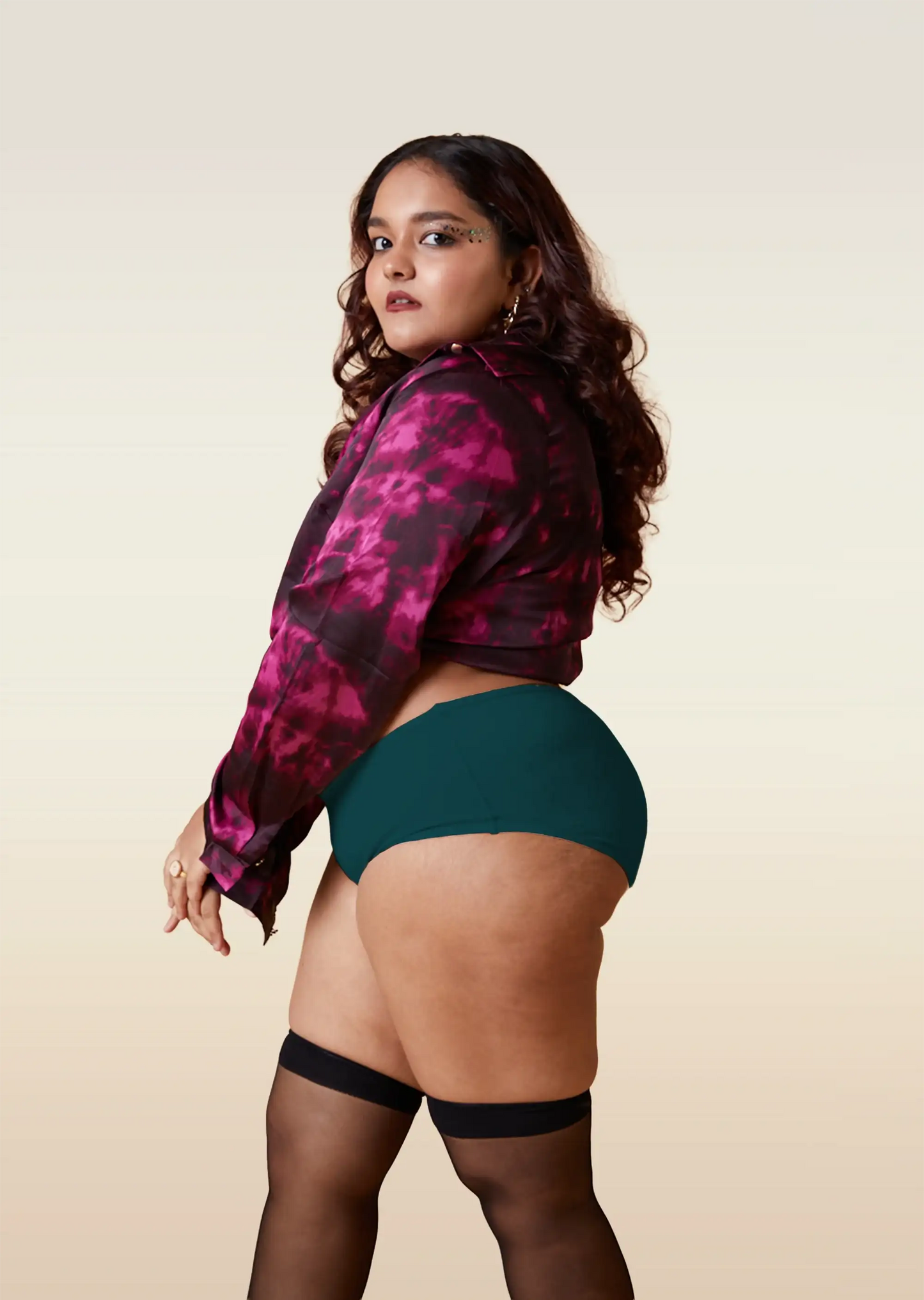 Woman wearing a pink and black patterned jacket, teal underwear, and black stockings on a beige background