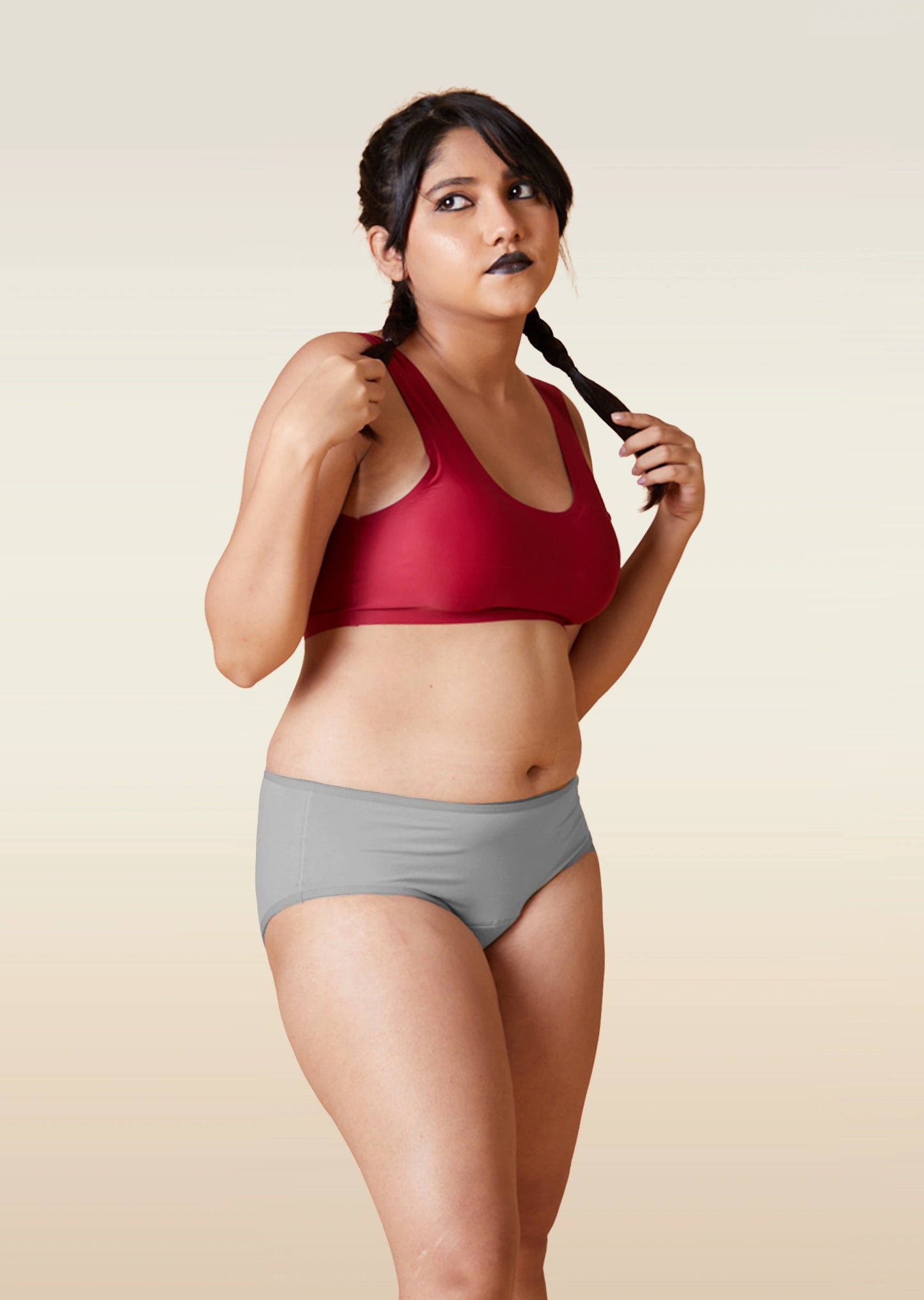 Woman wearing a red sports bra and gray underwear on a beige background