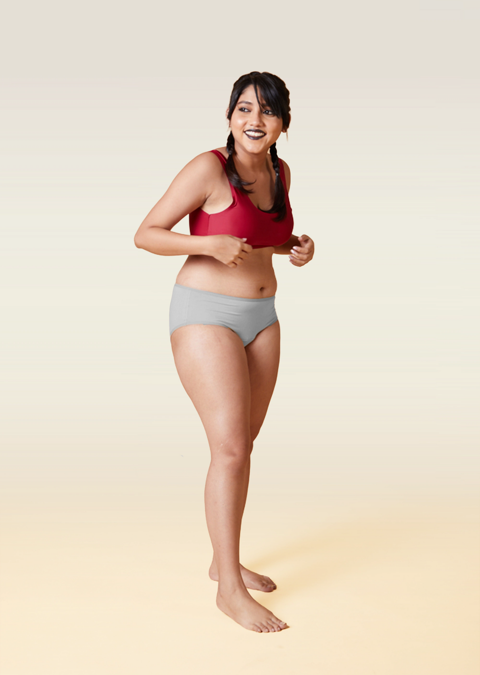 Woman wearing a red sports bra and gray underwear on a gradient background