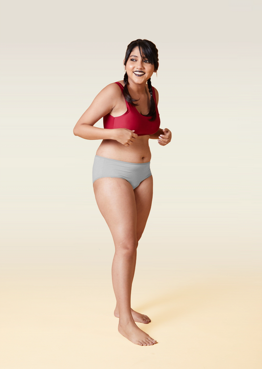 Woman wearing a red sports bra and gray underwear on a gradient background