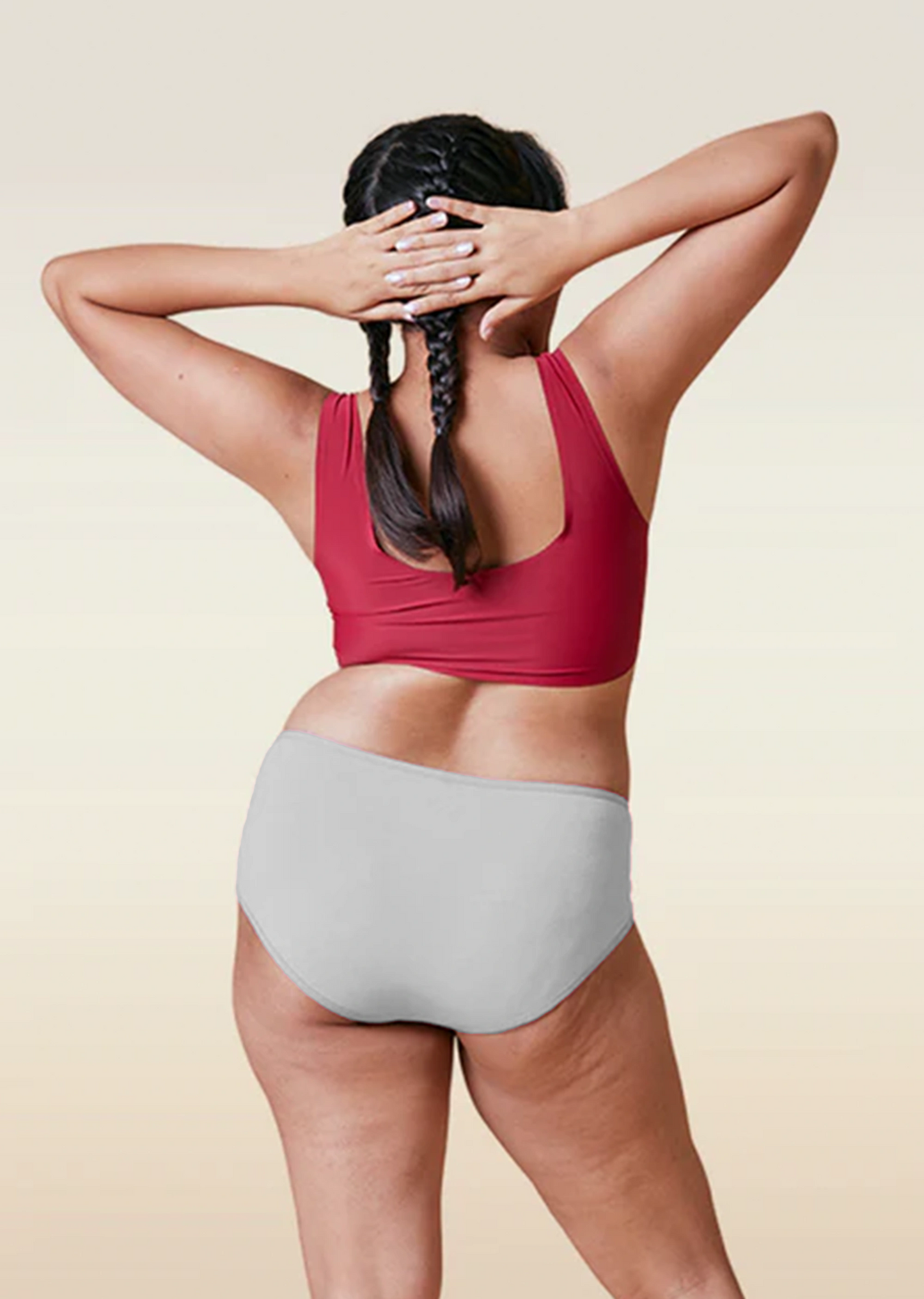 Person wearing a red sports bra and gray high-waisted underwear on a beige background