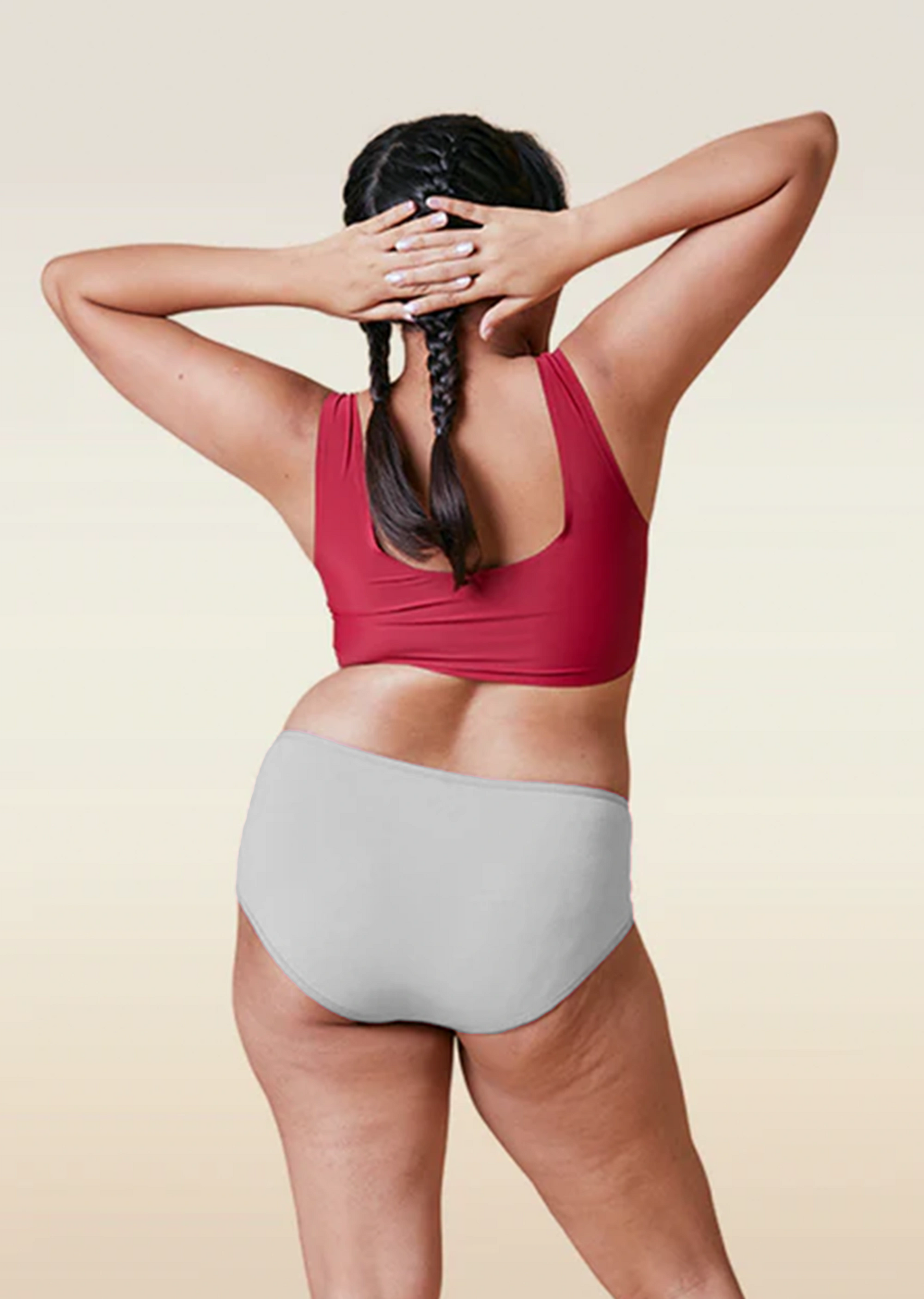 Person wearing a red sports bra and gray high-waisted underwear on a beige background