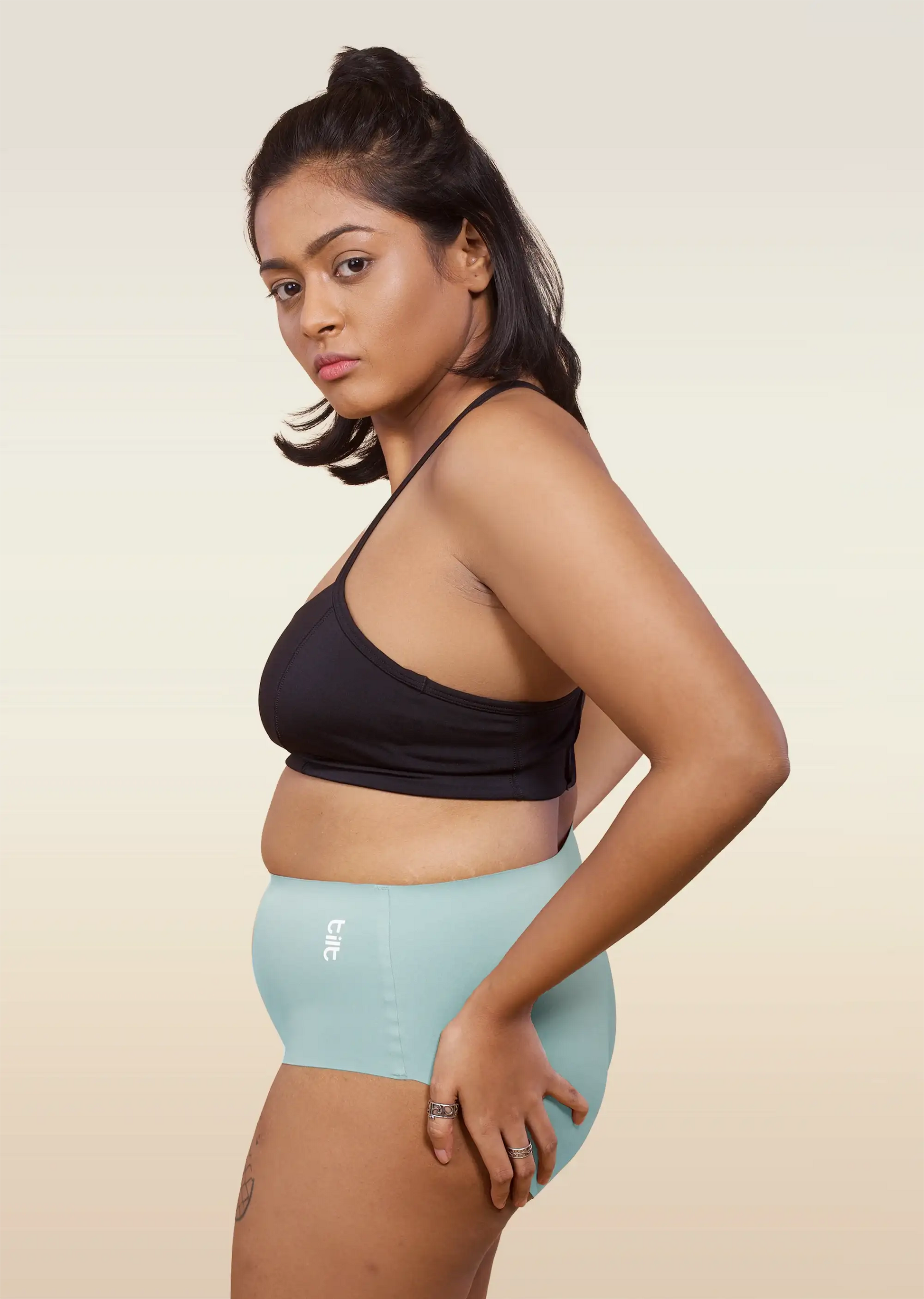 Woman wearing a black sports bra and light blue mid-waist underwear on a beige background