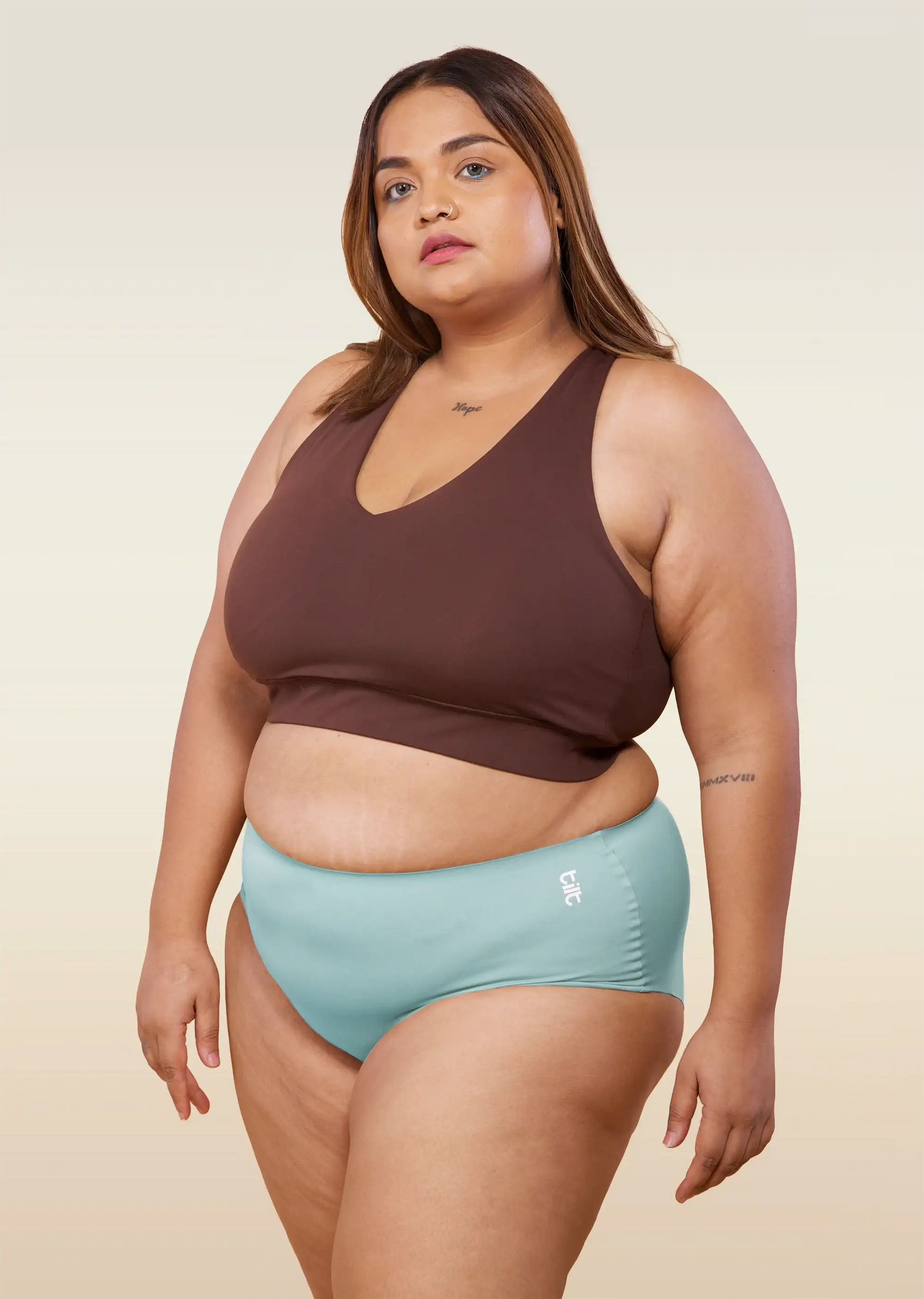 Woman wearing a brown sports bra and  blue mid-waist underwear on a beige background