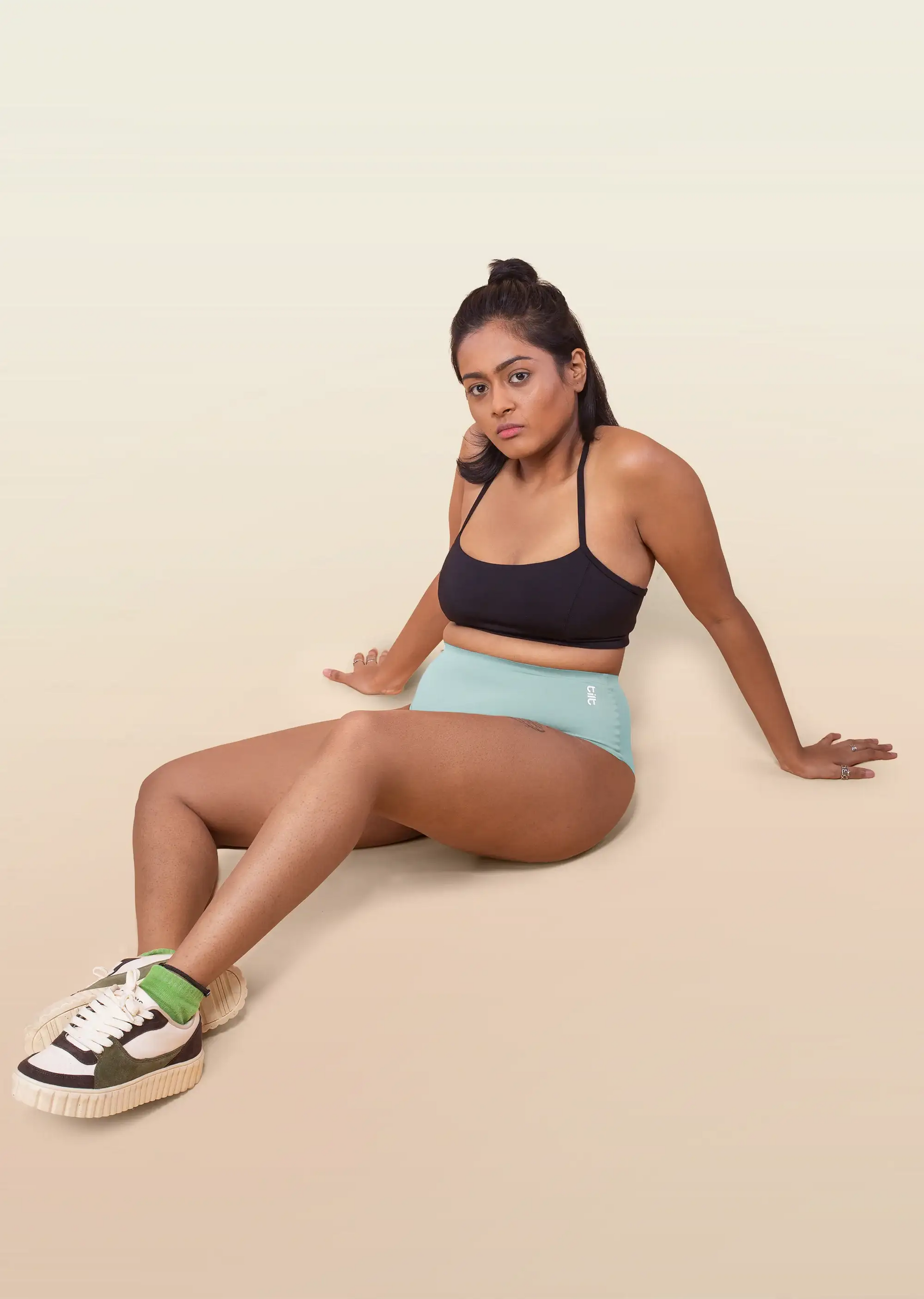 Woman sitting on a beige surface wearing a black sports bra and blue underwear