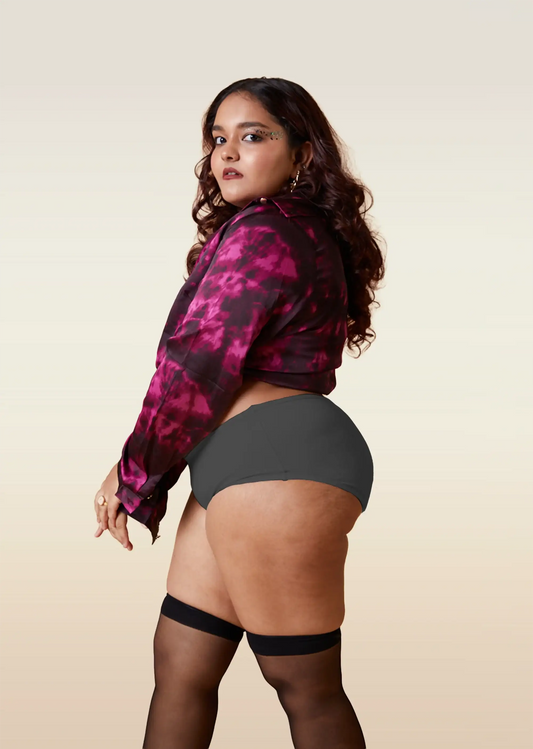 Woman wearing a pink and black patterned jacket with gray underwear and black stockings on a beige background